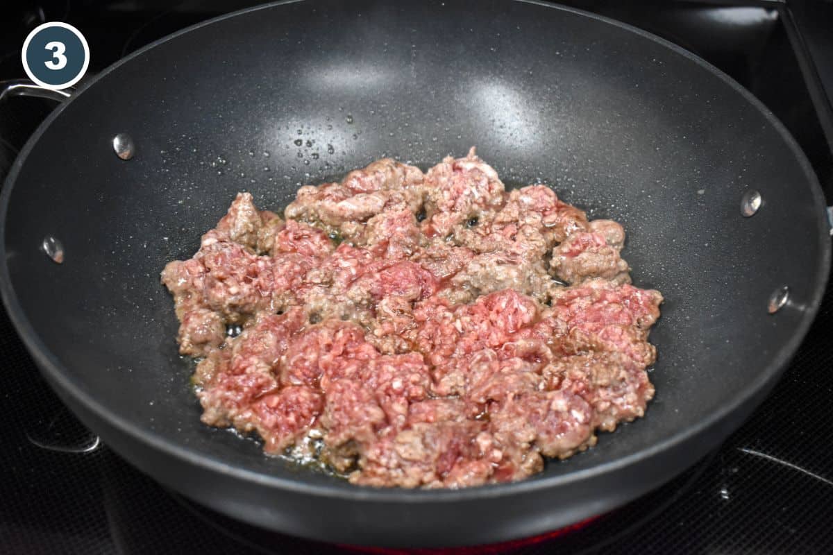 Ground beef browning in a large, black pan.