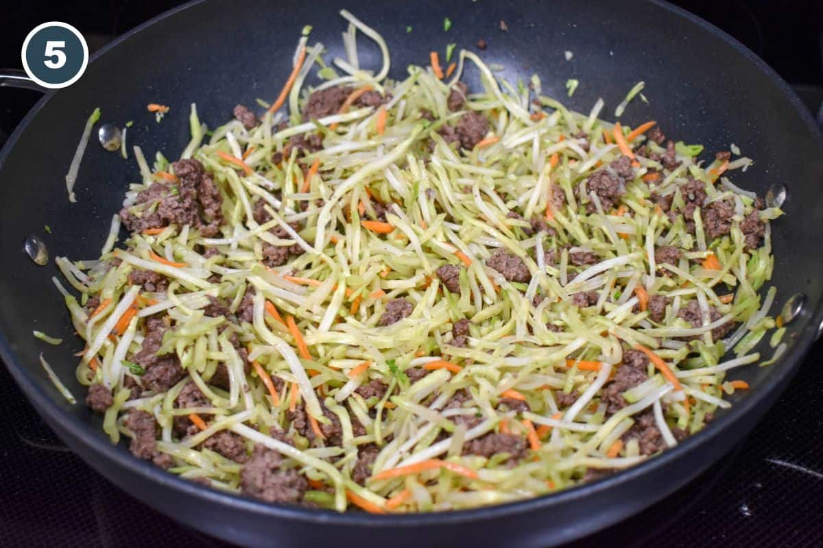 Ground beef and broccoli slaw in a large, black pan.