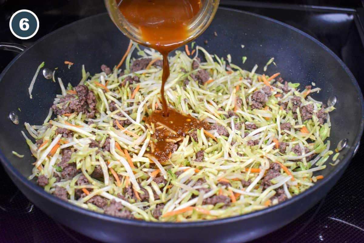 Stir fry sauce being poured on the beef and broccoli slaw in a large, black pan.