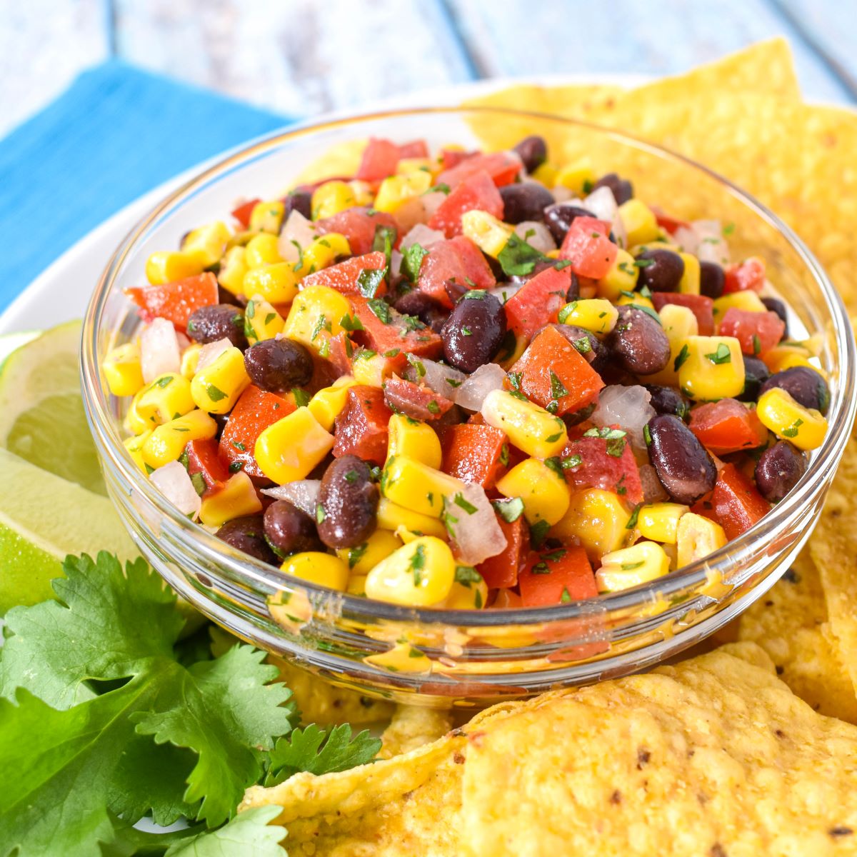 The finished dip served in a glass bowl with corn tortilla chips, lime wedges and a cilantro sprig on a white plate.