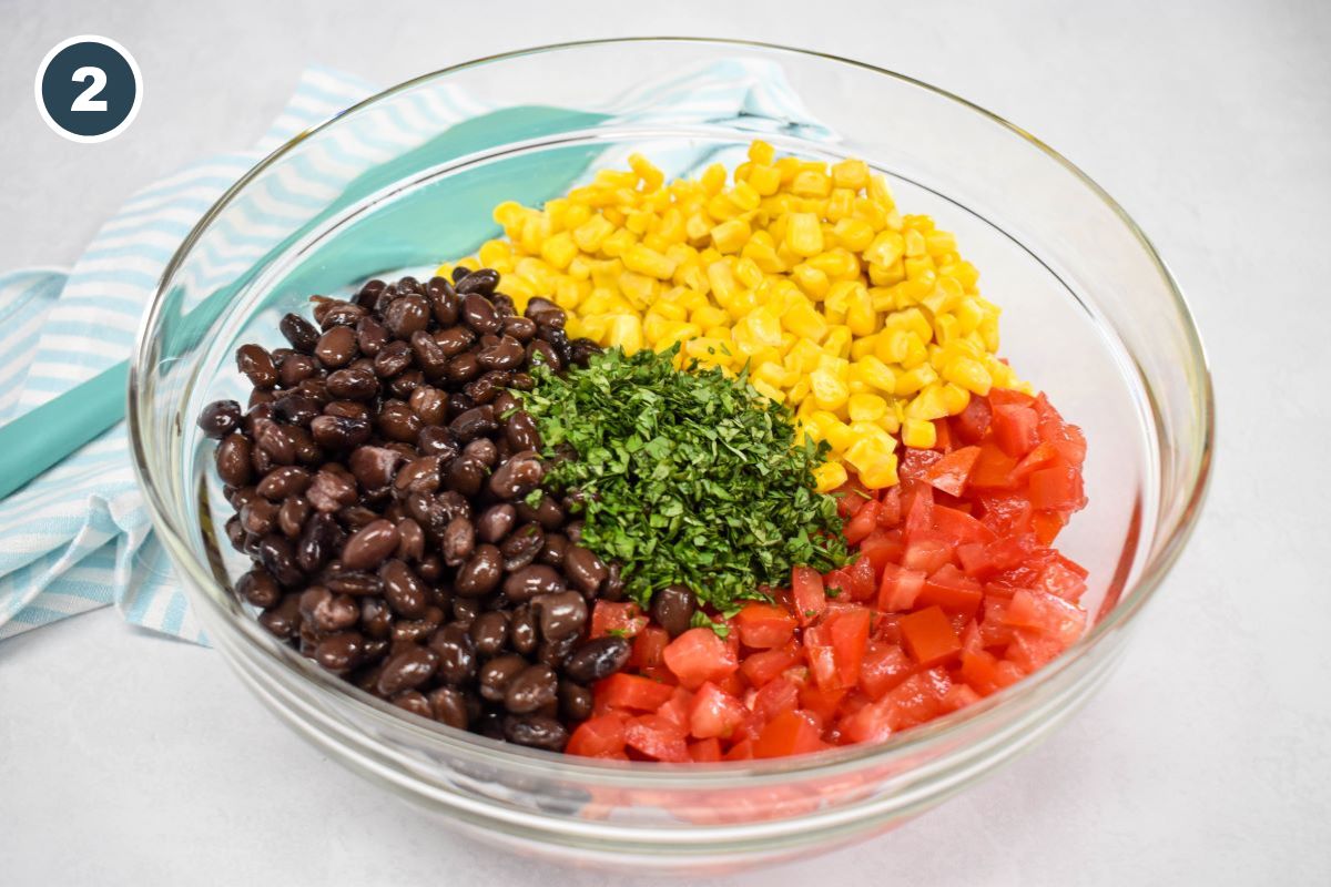 Black beans, corn, tomatoes, and cilantro added to a large glass bowl.