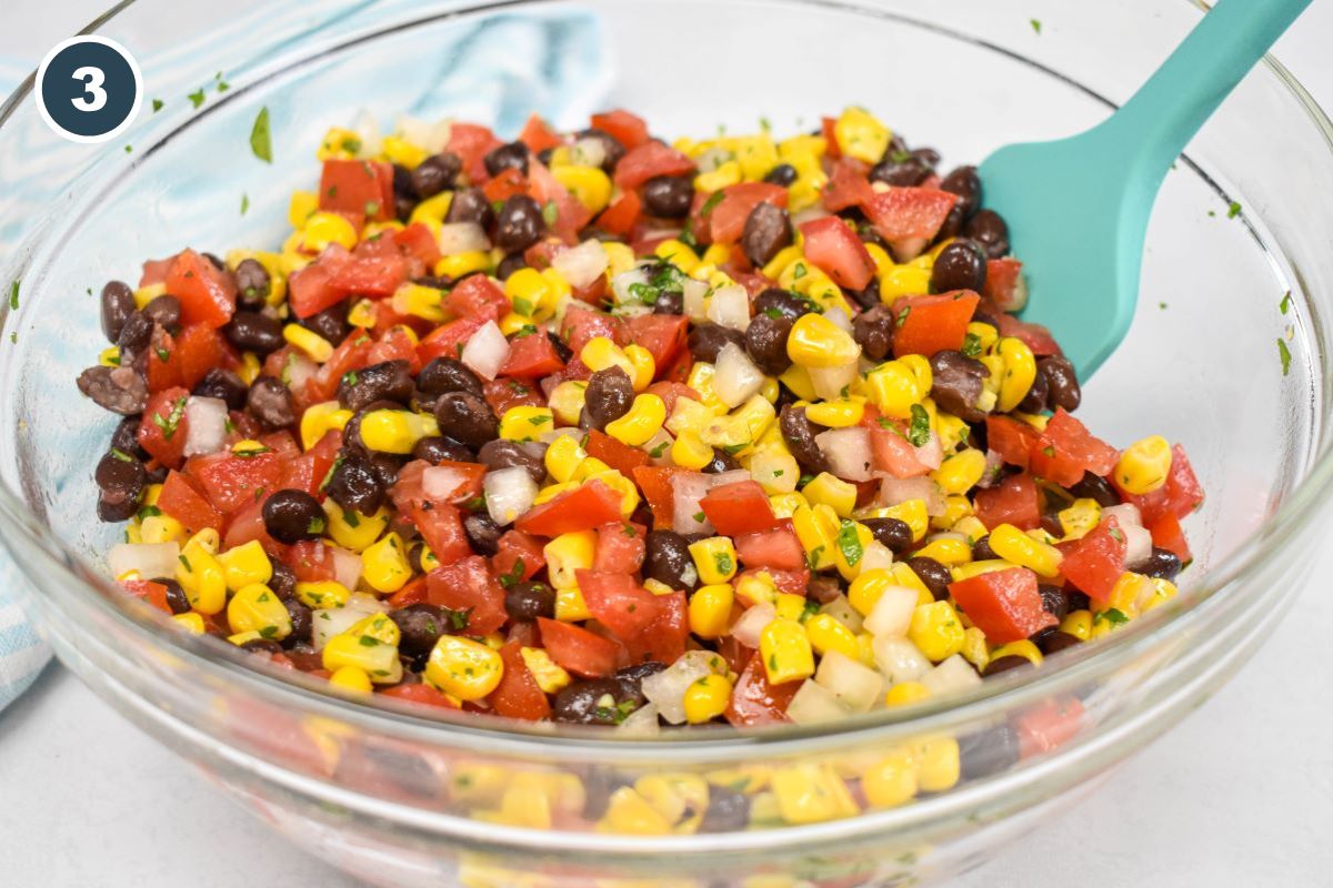 The salsa dip after combining in a large, glass bowl with a light blue spatula.