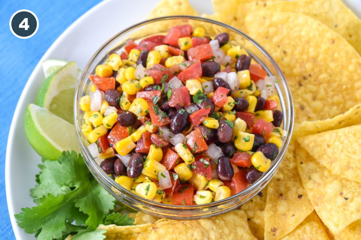 The finished dip served in a glass bowl with corn tortilla chips, lime wedges and a cilantro sprig on a white plate.