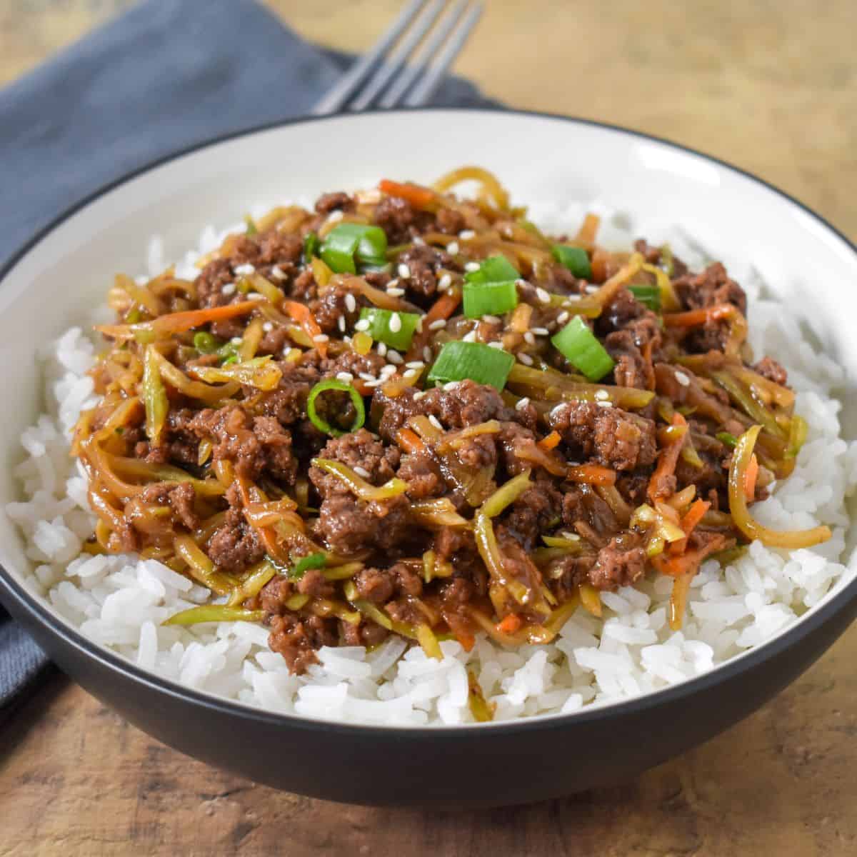 The finished stir fry served on a bed of white rice and garnished with sliced green onions and sesame seeds in a white bowl.