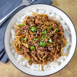 The ground beef stir fry served on a bed of white rice and garnished with sliced green onions and sesame seeds in a white bowl.