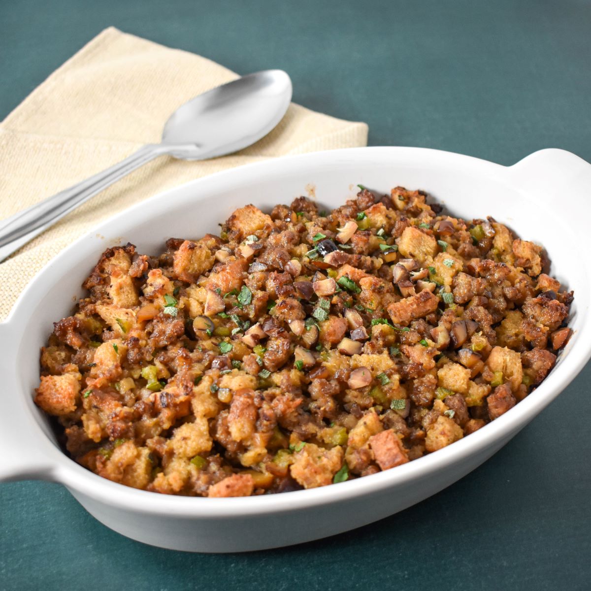 The chestnut sausage stuffing in a white casserole dish garnished with chopped parsley and sage.