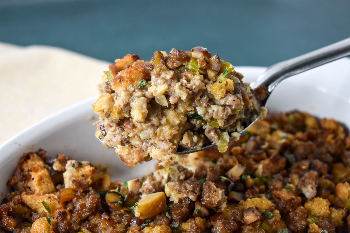 A scoopful of the stuffing lifted by a large serving spoon over the dish.