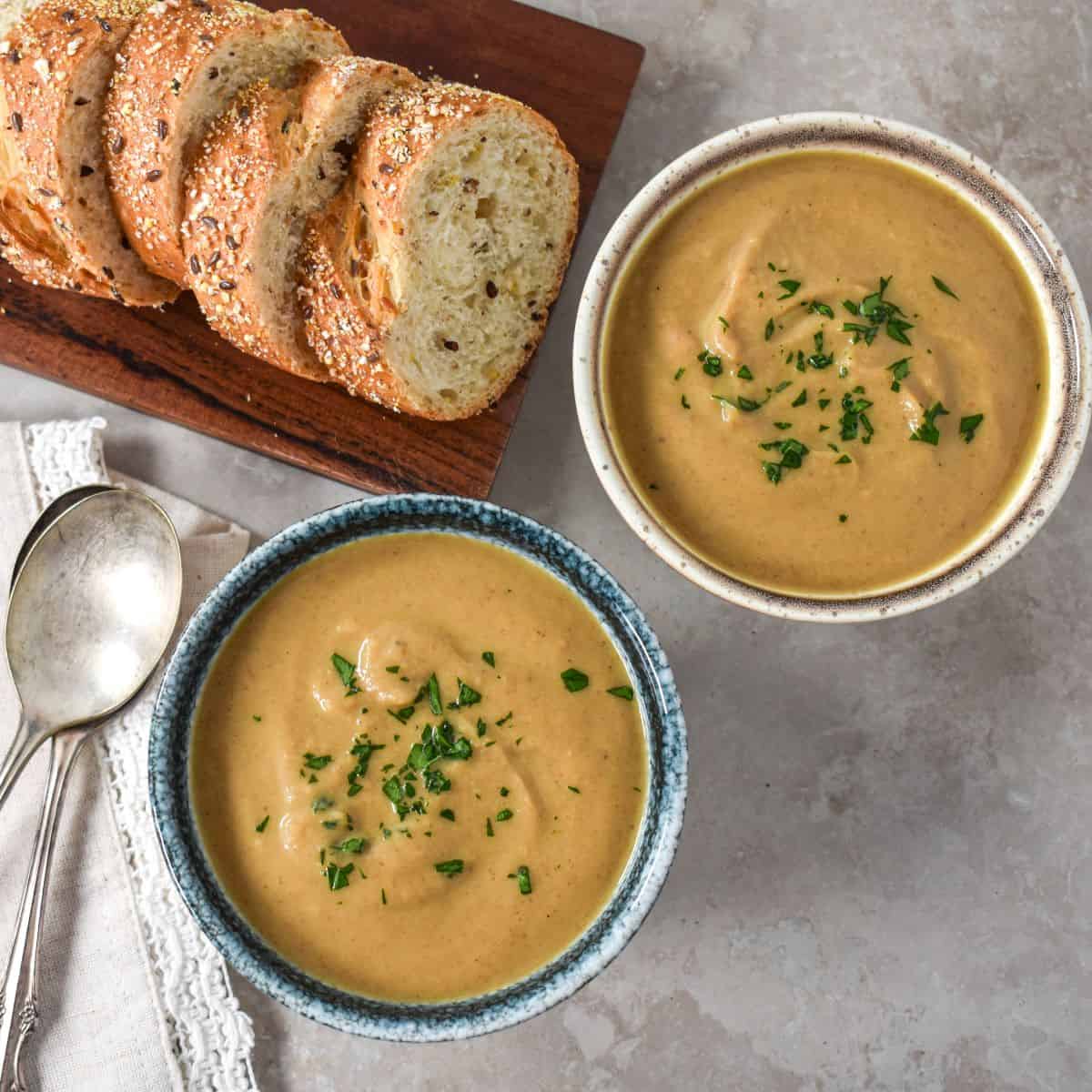 Two bowls of the finished soup with sliced bread in the background and two spoons to the left side.