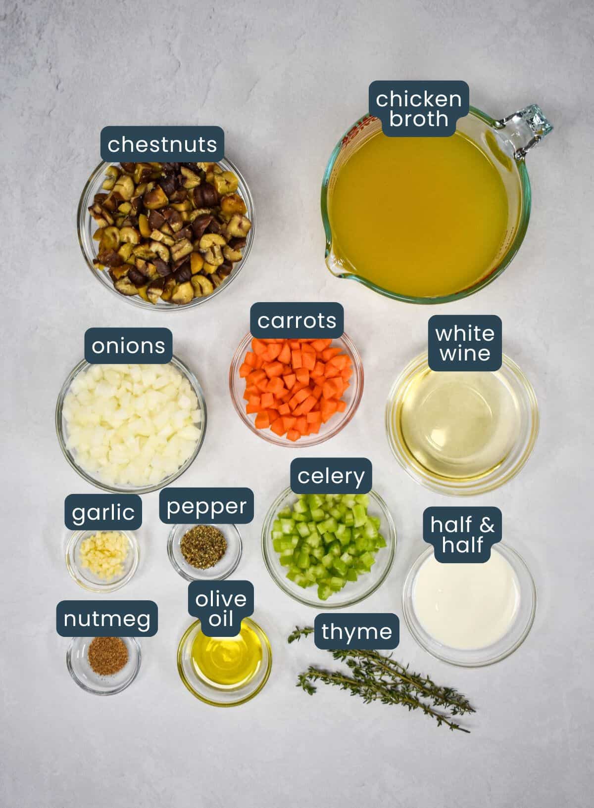 The ingredients for the soup prepped and arranged in glass bowls on a white table with each labeled with blue and white letters.