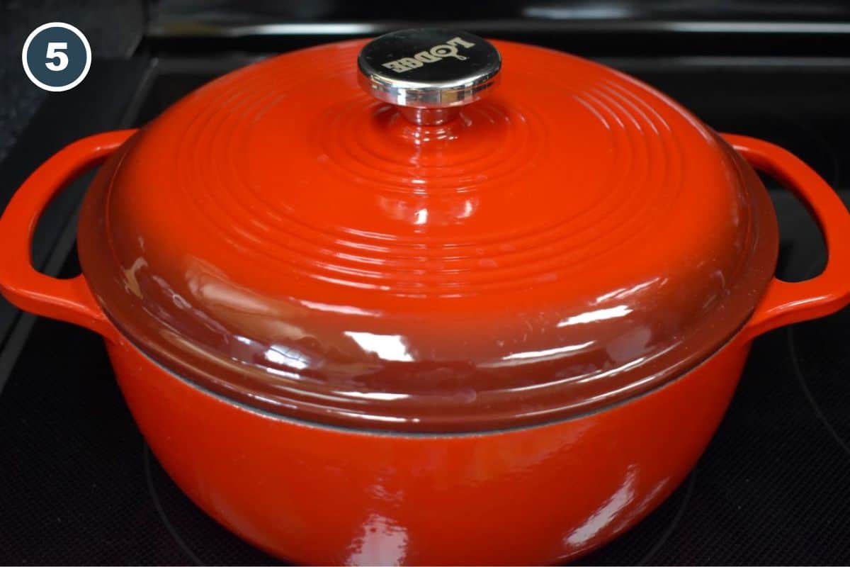 A covered red Dutch oven on a black stove.