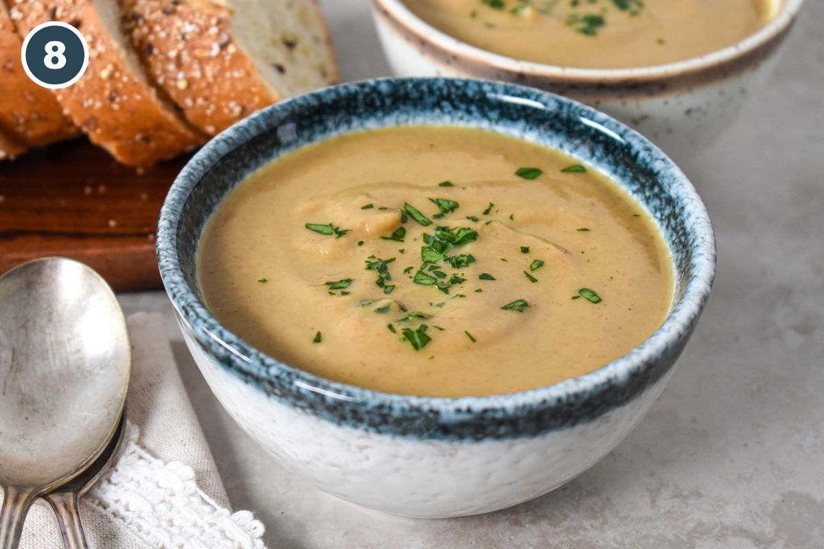 The soup, garnished with chopped parsley and served in a white bowl with a blue rim - a bowl and bread is partially visible in the background.