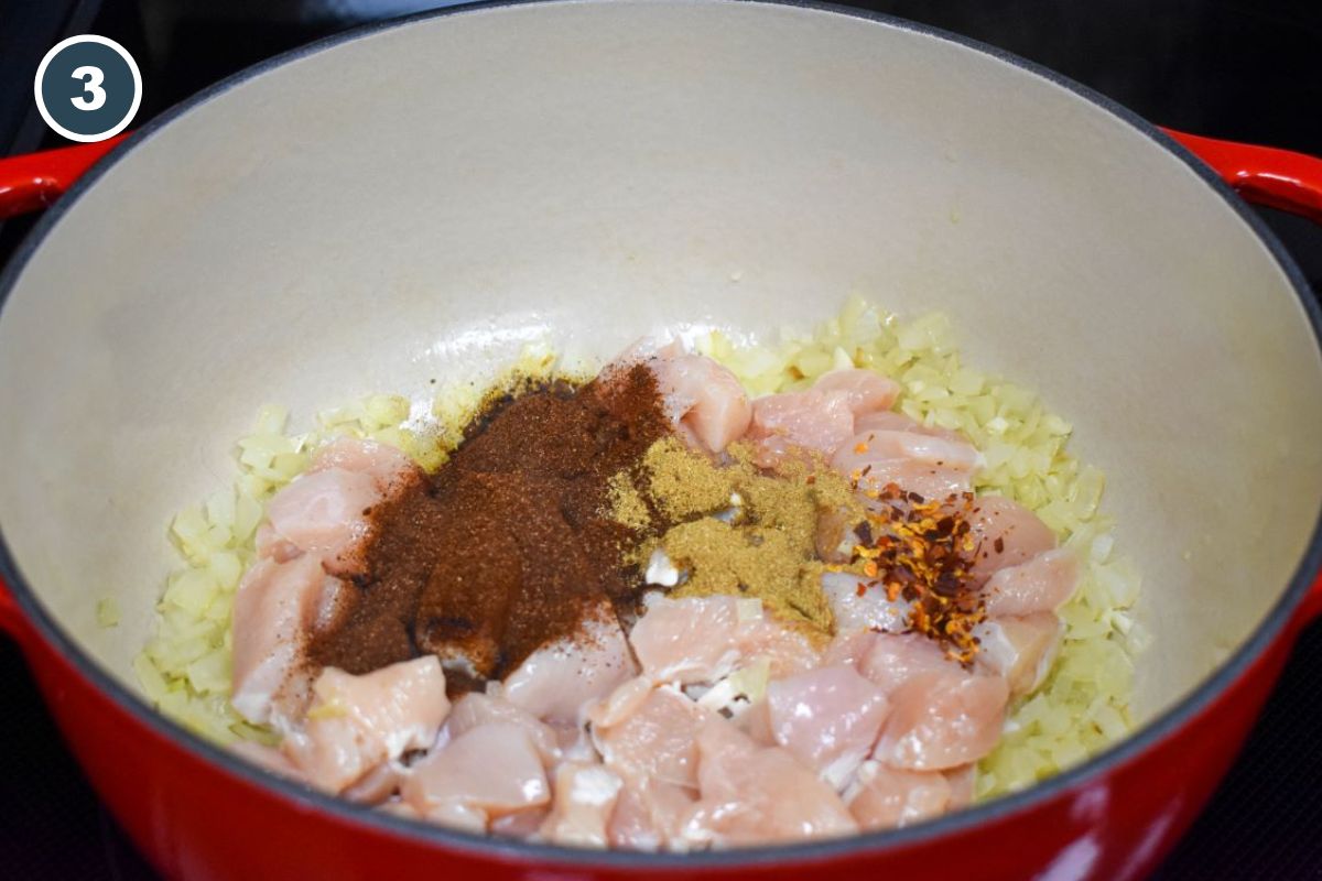 Chicken breast pieces and spices added to the onions in a pot.