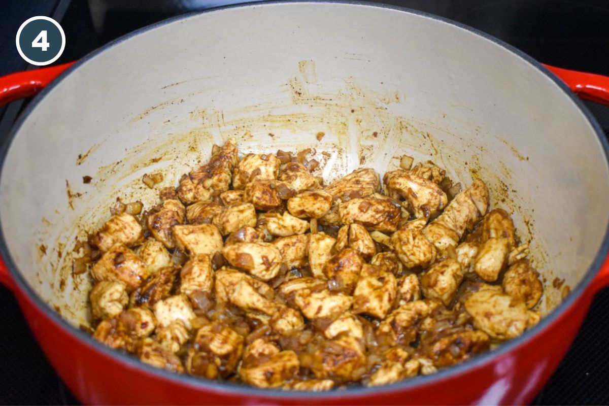 Seasoned, browned chicken pieces cooking with diced onions in a pot.