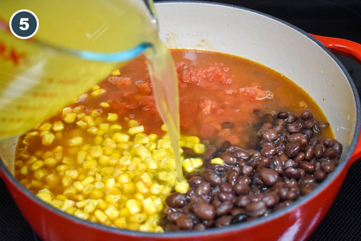 Diced tomatoes, corn, and black beans in the pot with chicken broth being added in.