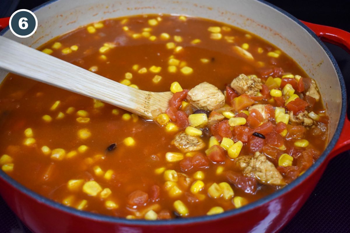 The soup in a large pot with a wooden spoon.