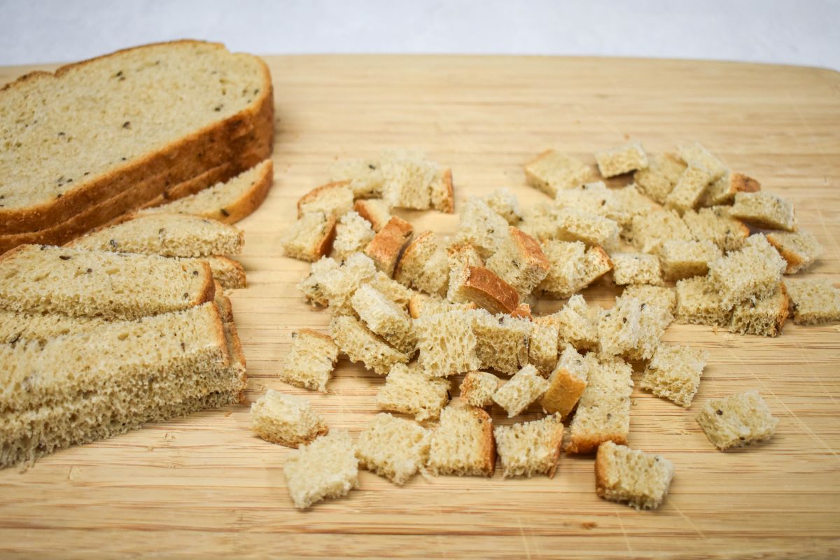 Rye bread in the process of being cut into cubes on a wood cutting board.