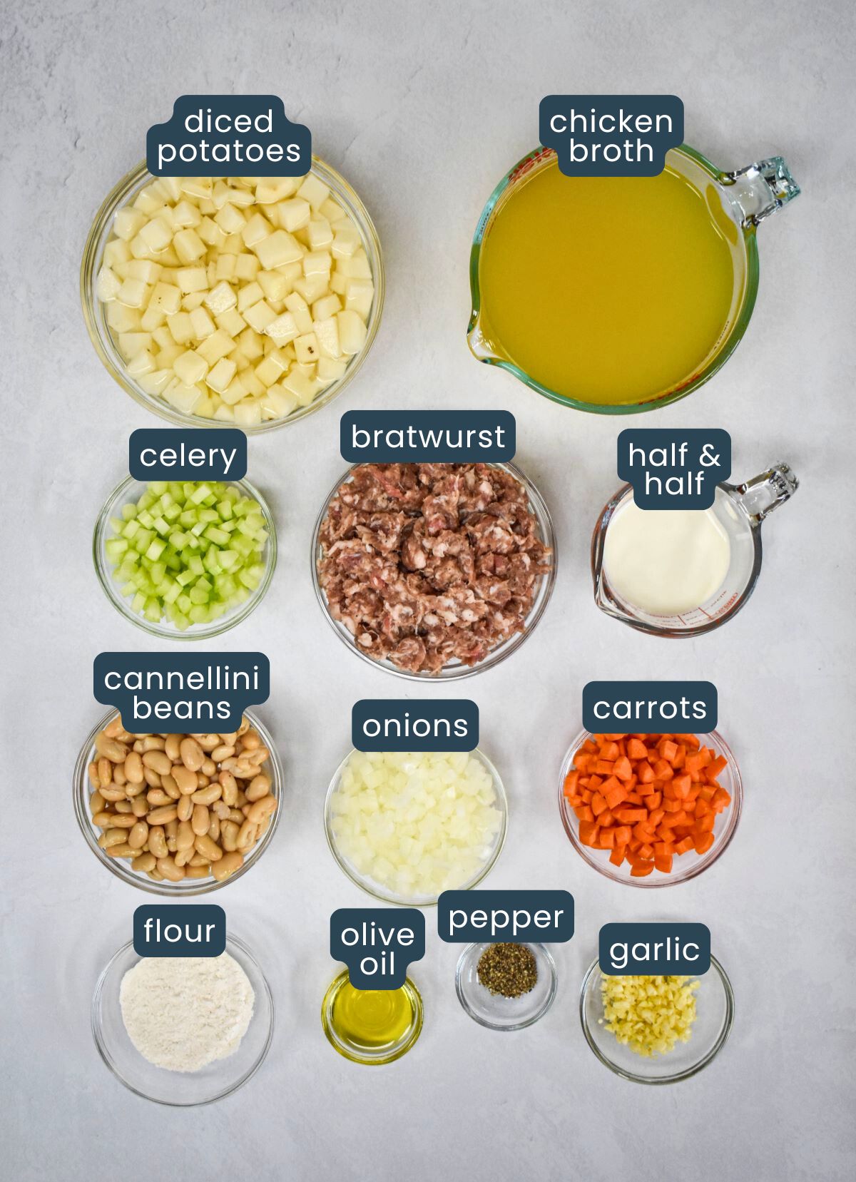 The ingredients for the soup prepped and arranged in glass bowls on a white table with each labeled.