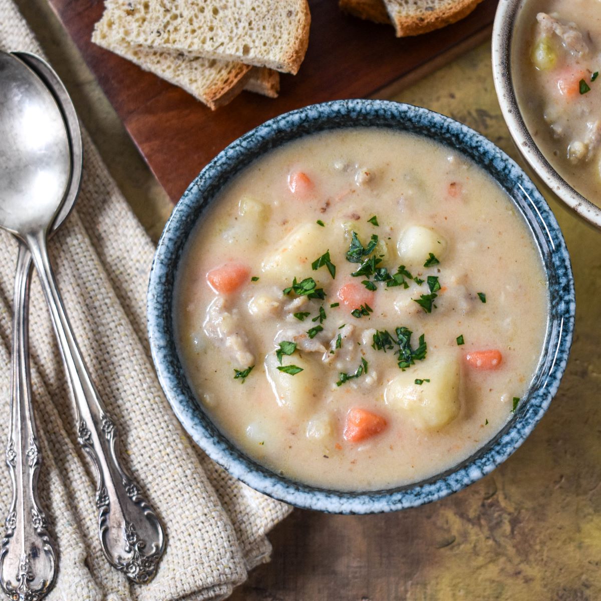 The bratwurst soup served in a blue bowl with sliced bread in the background.