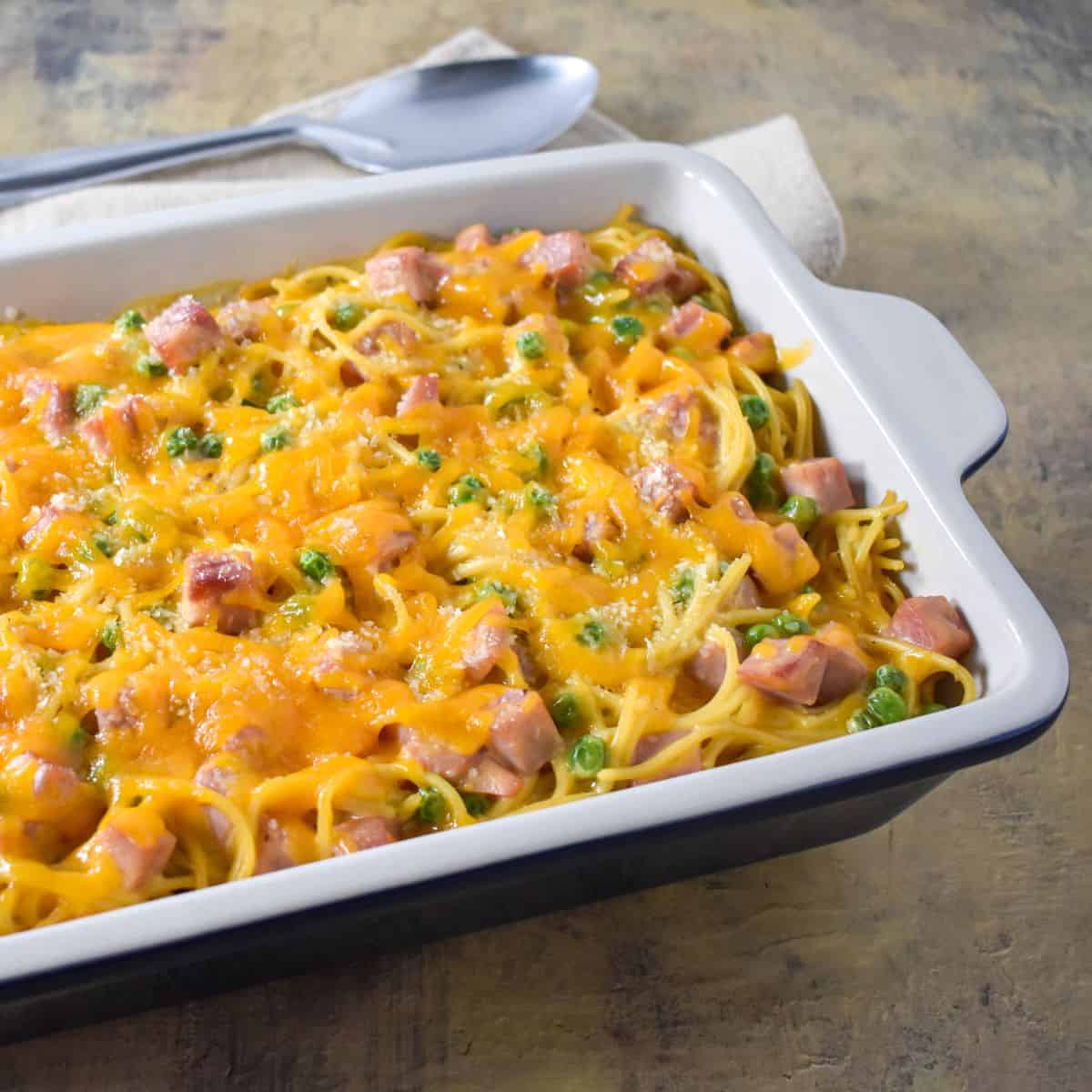 The finished baked pasta in a casserole dish with a beige linen and serving spoon.