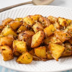 A close-up of French onion roasted potatoes served on a white plate, showing golden-brown edges, caramelized onions, and fresh herbs.