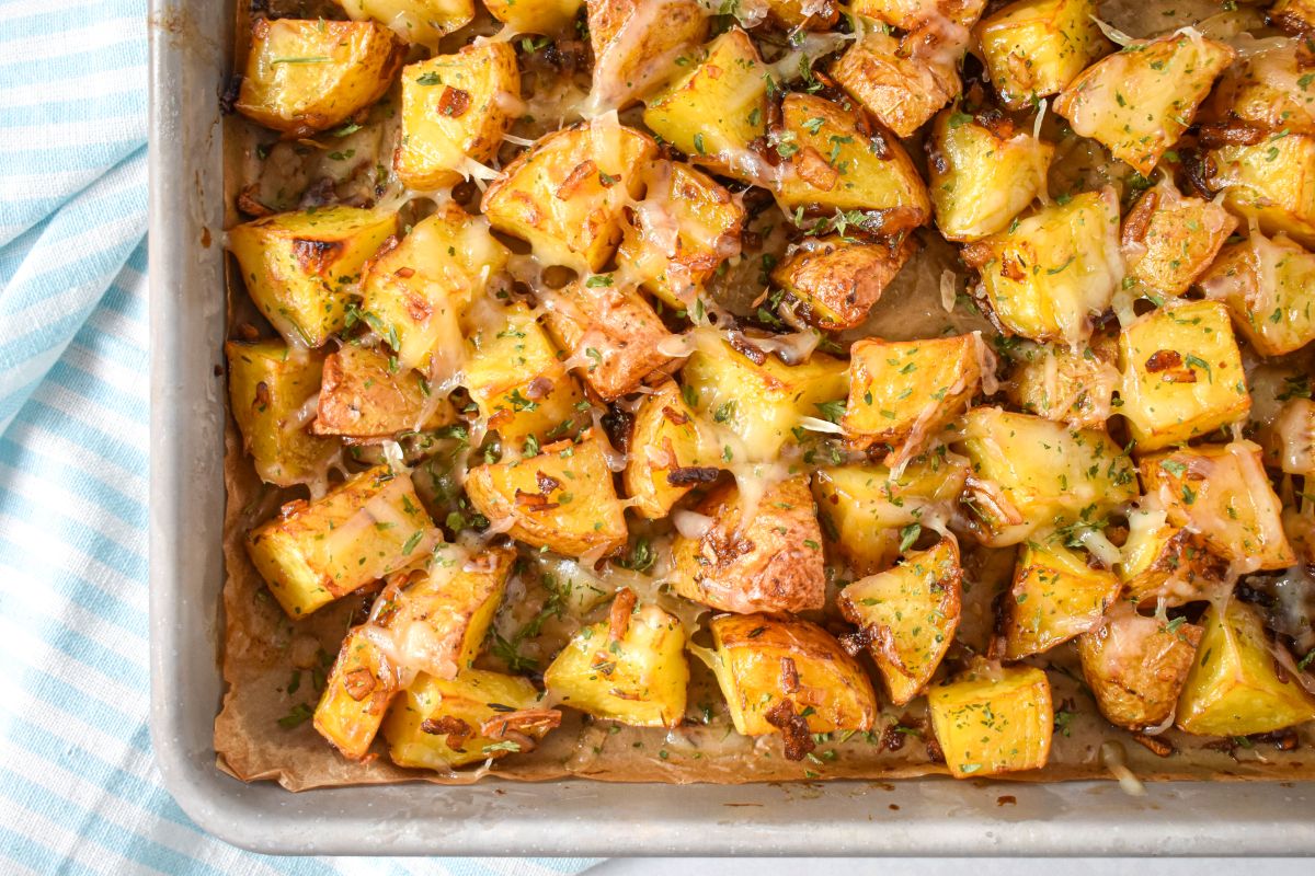 French onion roasted potatoes on a parchment-lined baking sheet, topped with melted cheese and herbs.