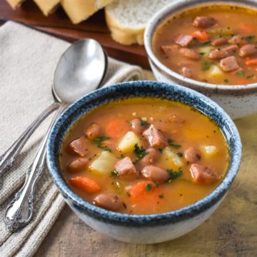 Two small bowls of the ham and pinto bean soups served with sliced bread.