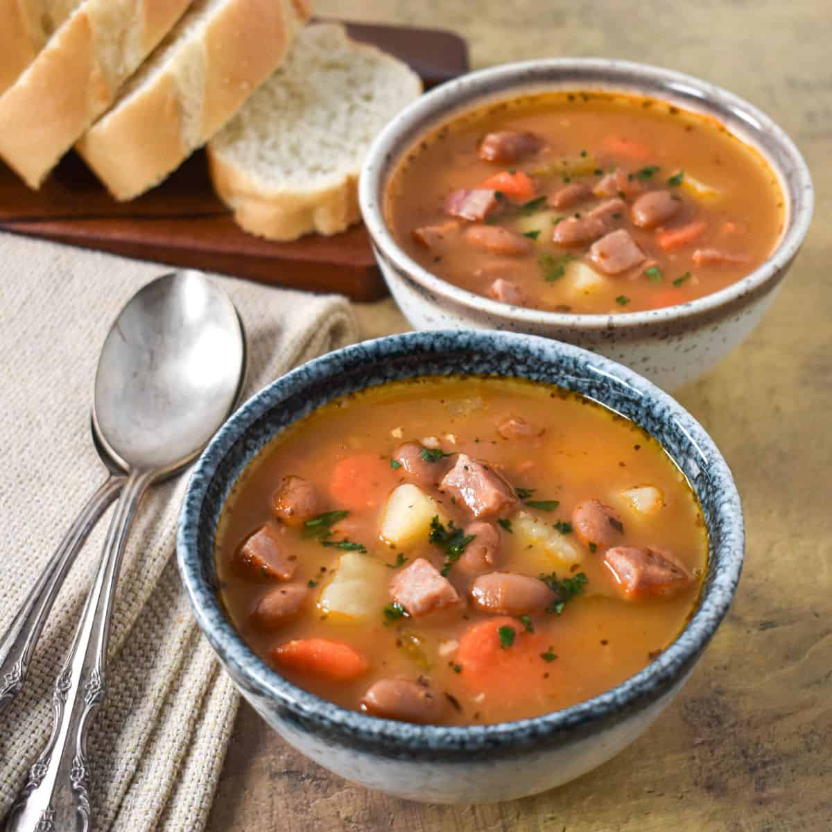 Two small bowls of the ham and pinto bean soups served with sliced bread.