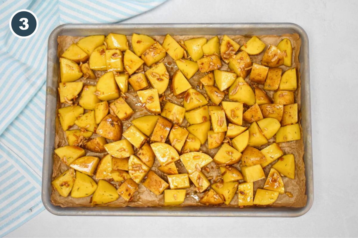 Seasoned potato cubes spread in a single layer on a parchment-lined baking sheet, ready to roast.