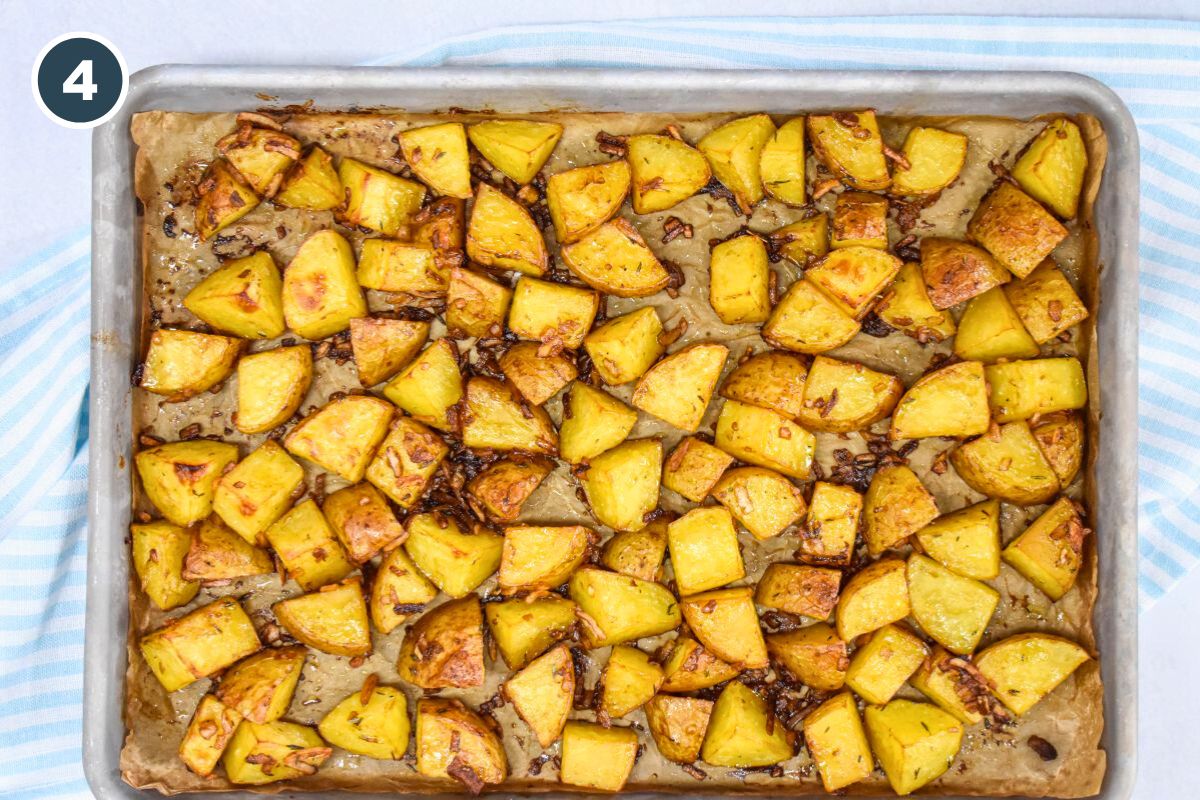 Golden brown roasted potatoes on a parchment-lined baking sheet, with crispy onion bits.