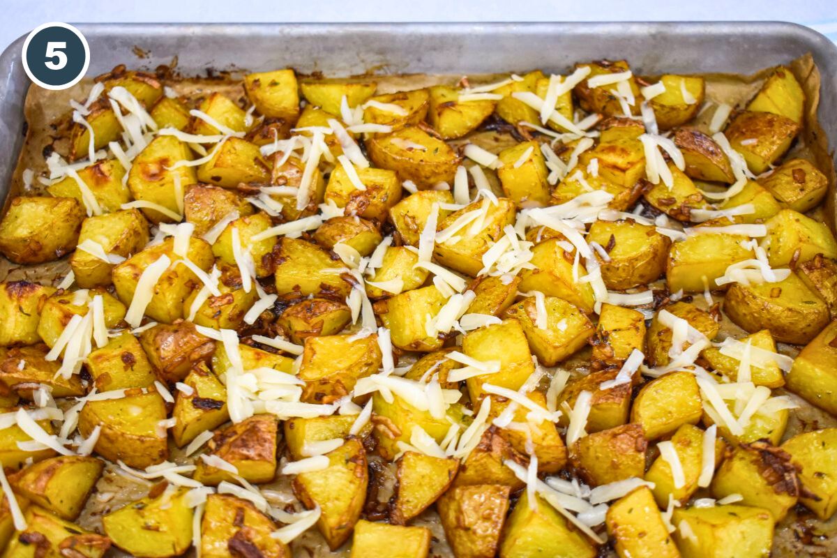 Shredded Swiss cheese sprinkled over roasted potatoes on a baking sheet, before melting.