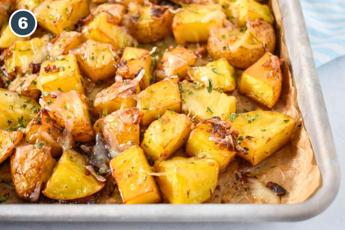 Roasted potatoes with melted cheese and fresh herbs on a baking sheet, ready to serve.