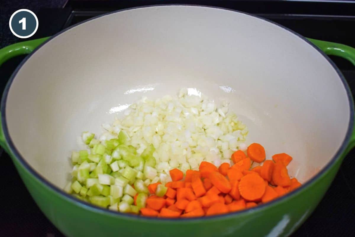 Diced onions, carrots, and celery in a large green and white Dutch oven.