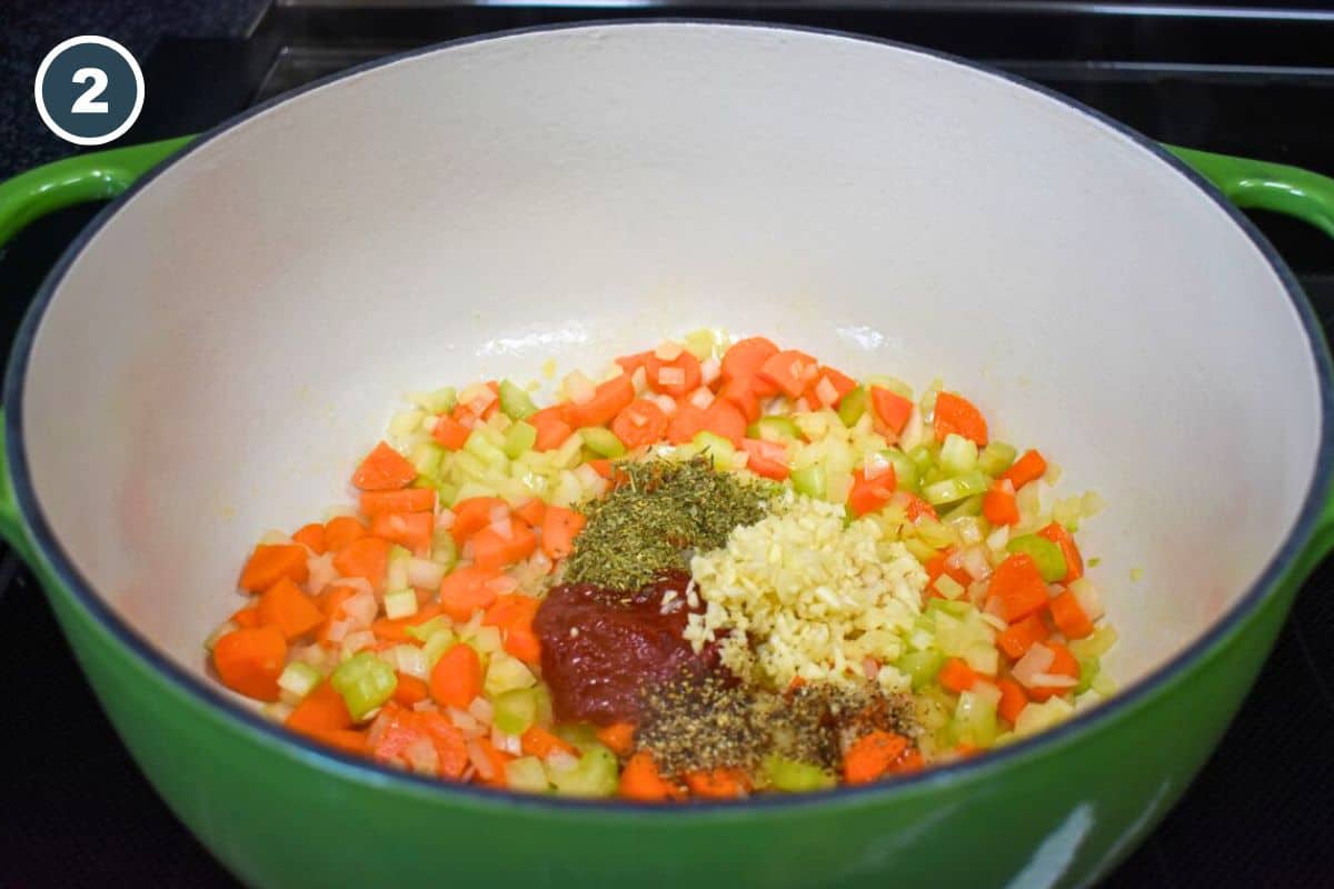 Garlic, seasonings, and tomato paste added to the sauteed onions, carrots, and celery in the pot.