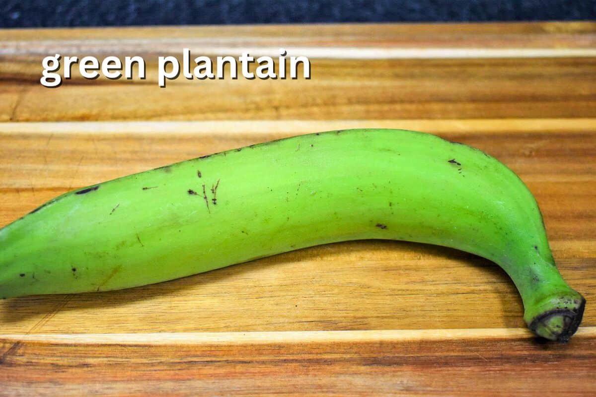 A whole green plantain on a wooden cutting board, labeled "green plantain."