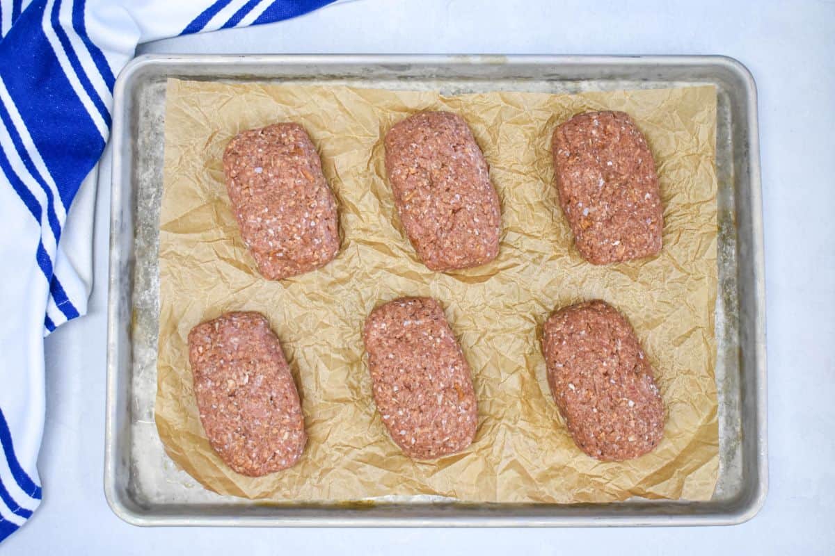 3- Six raw mini turkey meatloaves shaped and placed on a parchment-lined baking sheet, ready for baking.