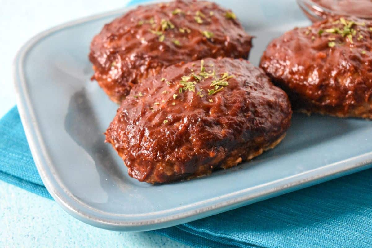 Glazed mini turkey meatloaves garnished with parsley, served on a blue plate with a blue napkin underneath.